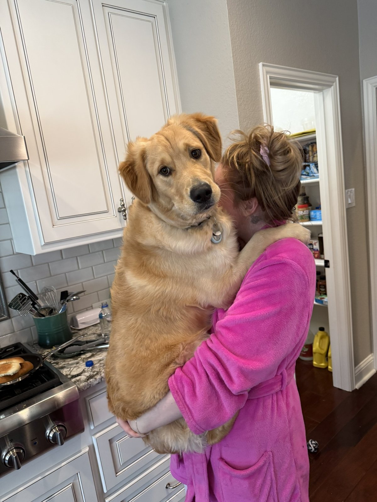 Winnie's mom in a pink robe holding Winnie in the kitchen.